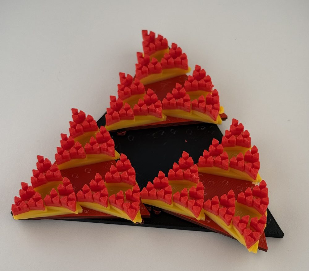 3D printed triangle made of smaller triangles covered in red peaks, on a black base